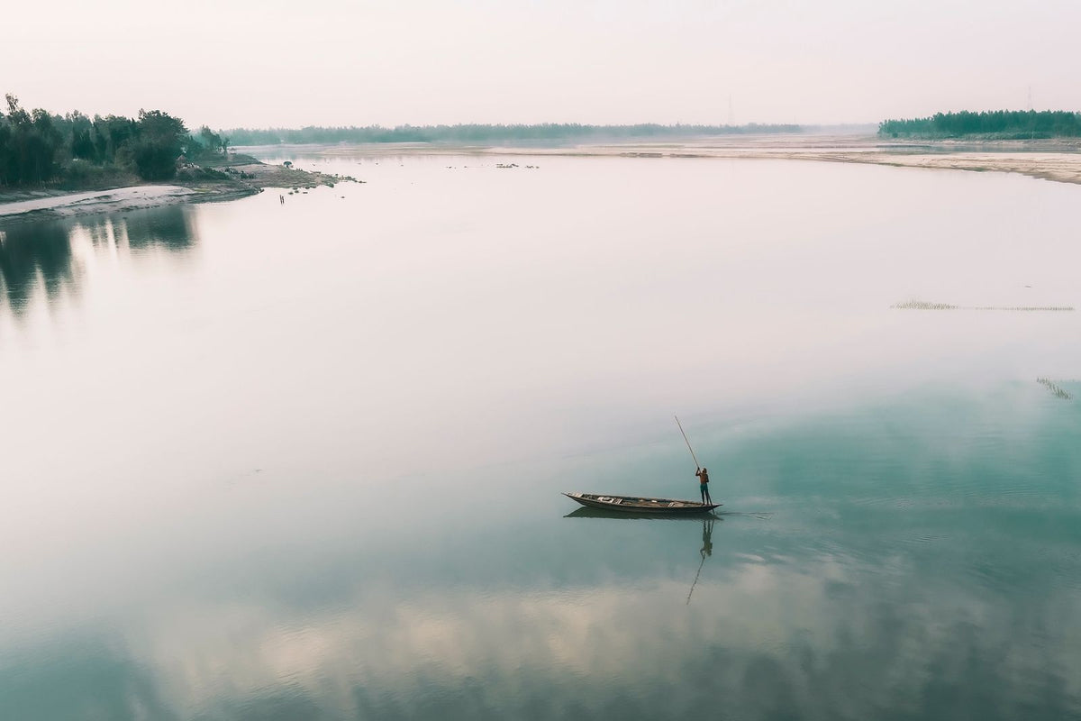 A lone angler in a small boat on wide, calm water at first light